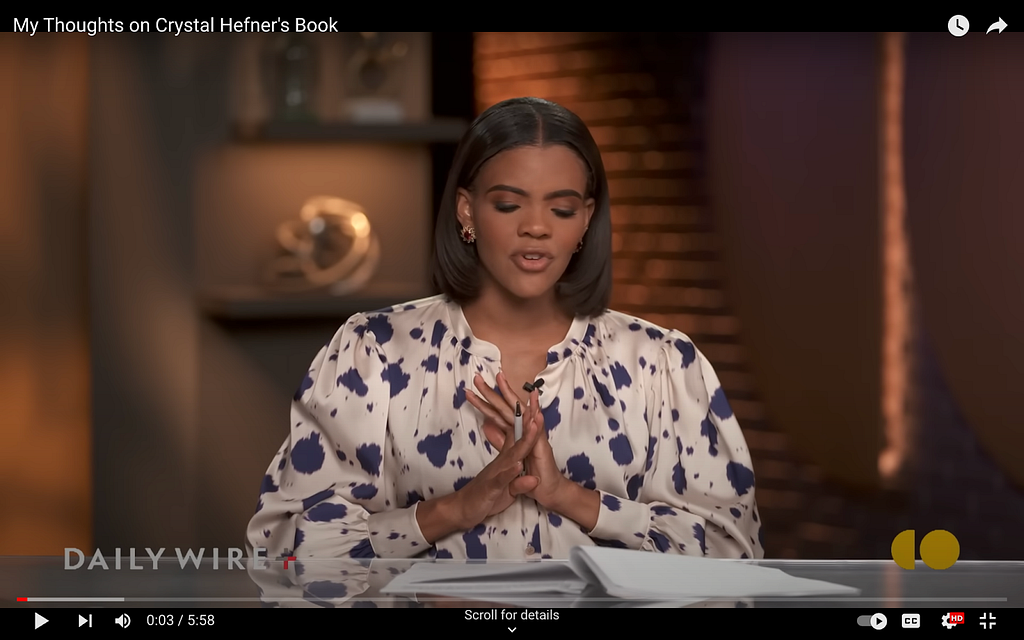 A screenshot from Candace Owens’s show on The Daily Wire. She wears a billowy, silky blouse with a button undone around the collarbone. It’s ivory with splotches of navy blue all over it which makes her look like a fancy cow.