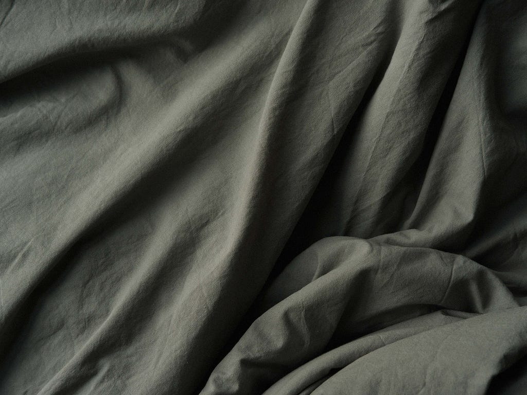 Photo of a grey sheet, draped with uneven folds & bunched in one corner