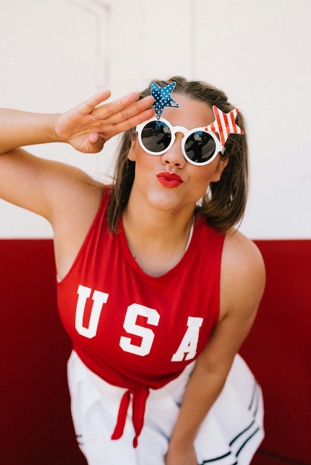 woman in red white and blue clothing and funny sunglasses saluting