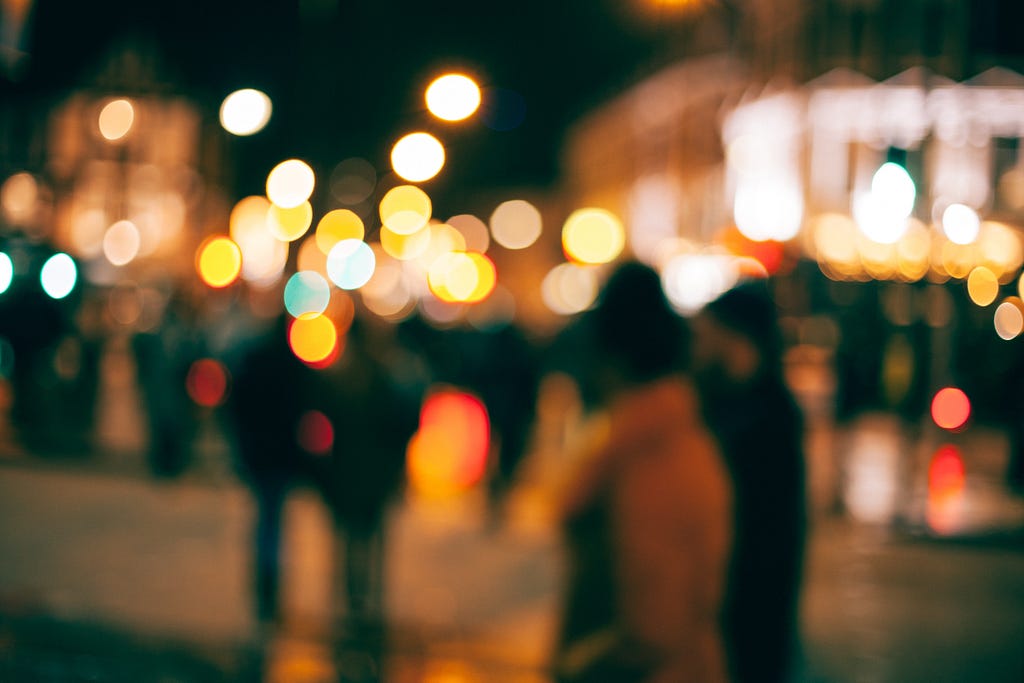 Highly blurred photo of people on the street in a city at night.