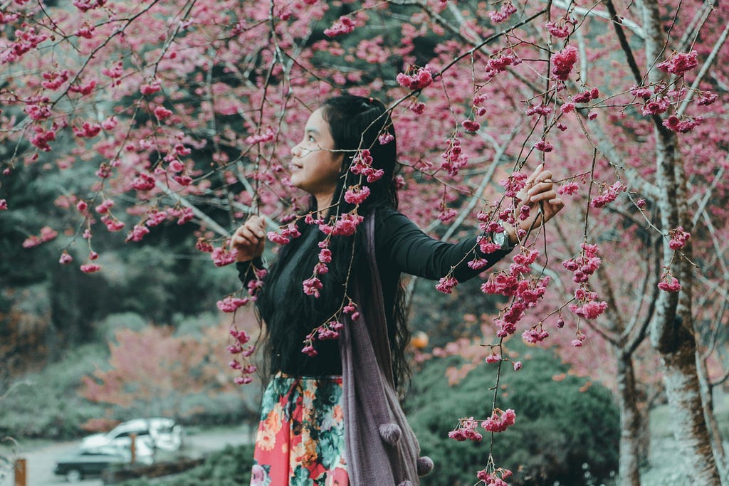 female standing beside a blossoming tree with her hands running through the branches