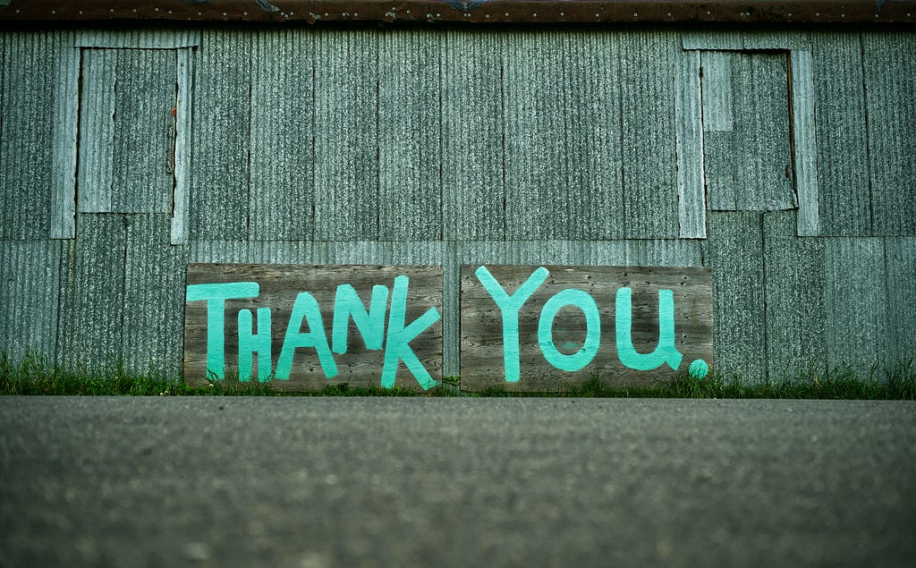 Painted blue thank you on a grey barn wall