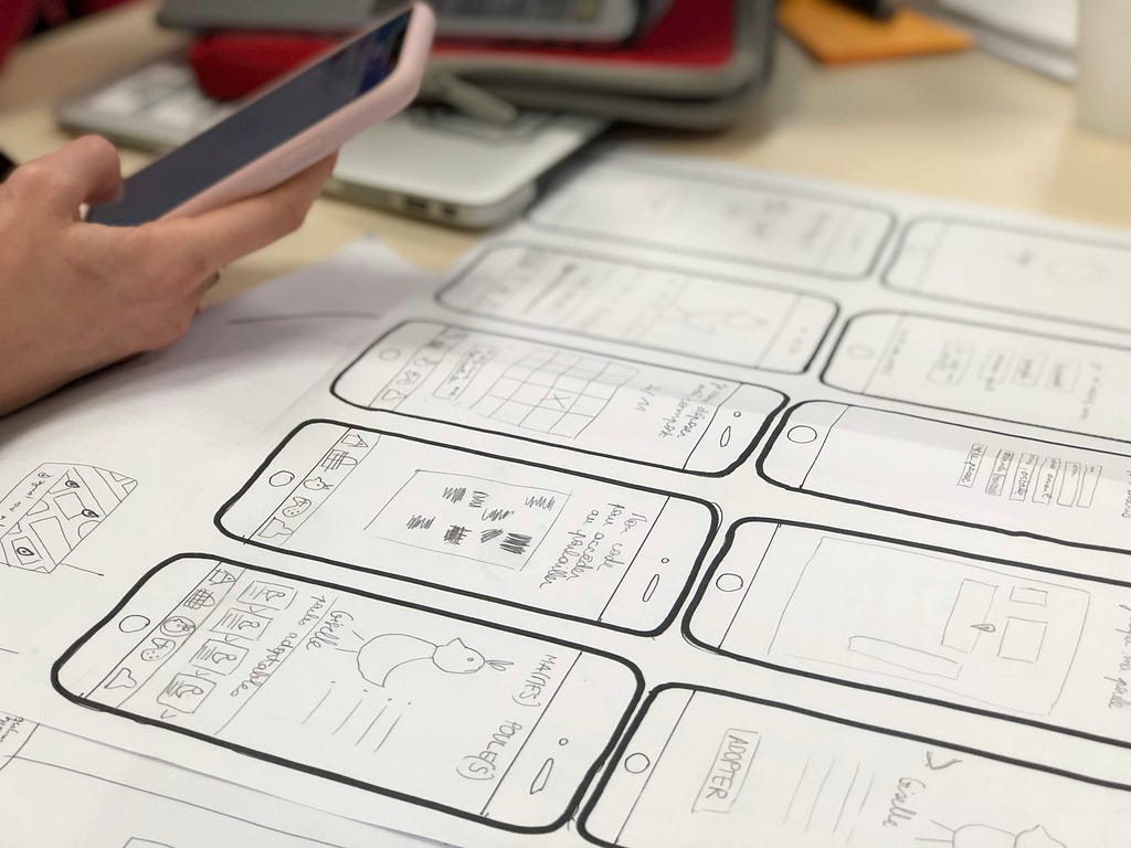A person takes a photo with their camera phone of a series of hand-drawn prototype sketches for a mobile app.