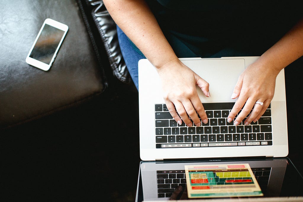 Person’s hands typing on a laptop with a mobile phone next to them.