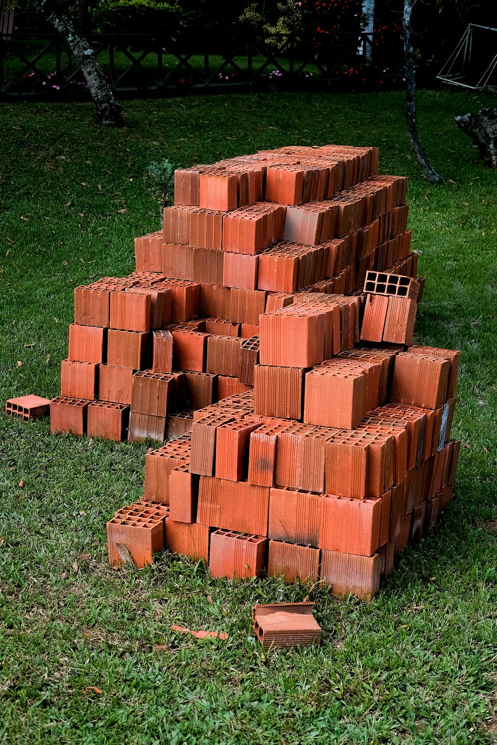 A photograph of a pile of bricks stacked on a lawn. Photo by Matt W Newman on Unsplash.