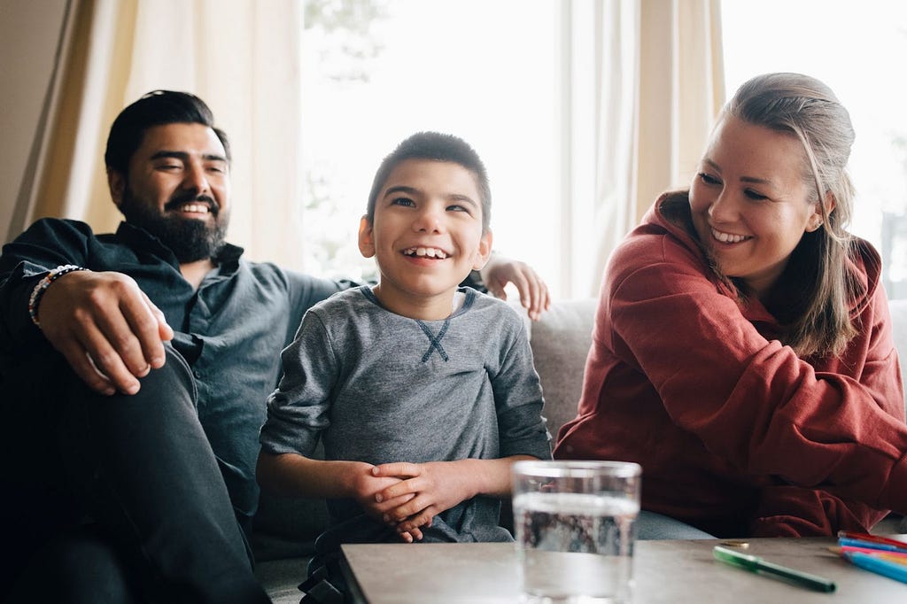 Child with rare disease smiles while sitting on couch with parents