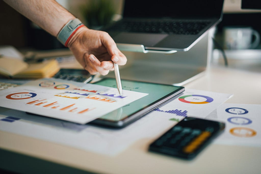 A person analyzing data charts and graphs on a tablet and paper, surrounded by a laptop and calculator, highlighting the power of augmented analytics in business.