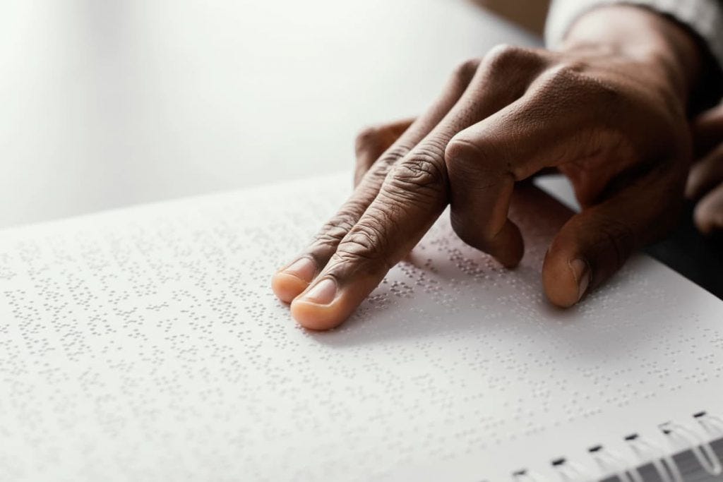 Image from Freepik of a man’s hand on a page of braille