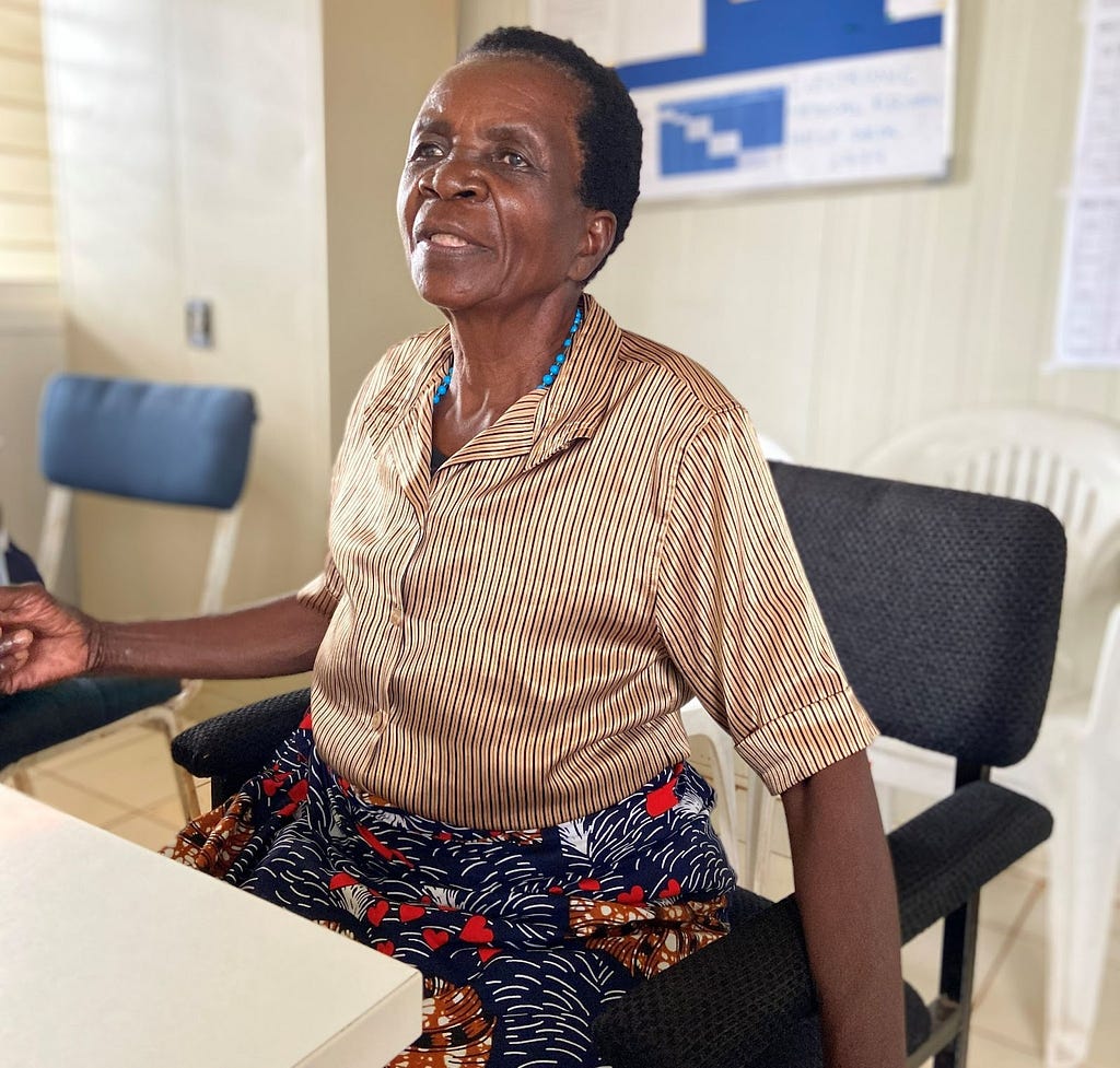 A woman sits in a chair and gestures with her arms as she tells her story.