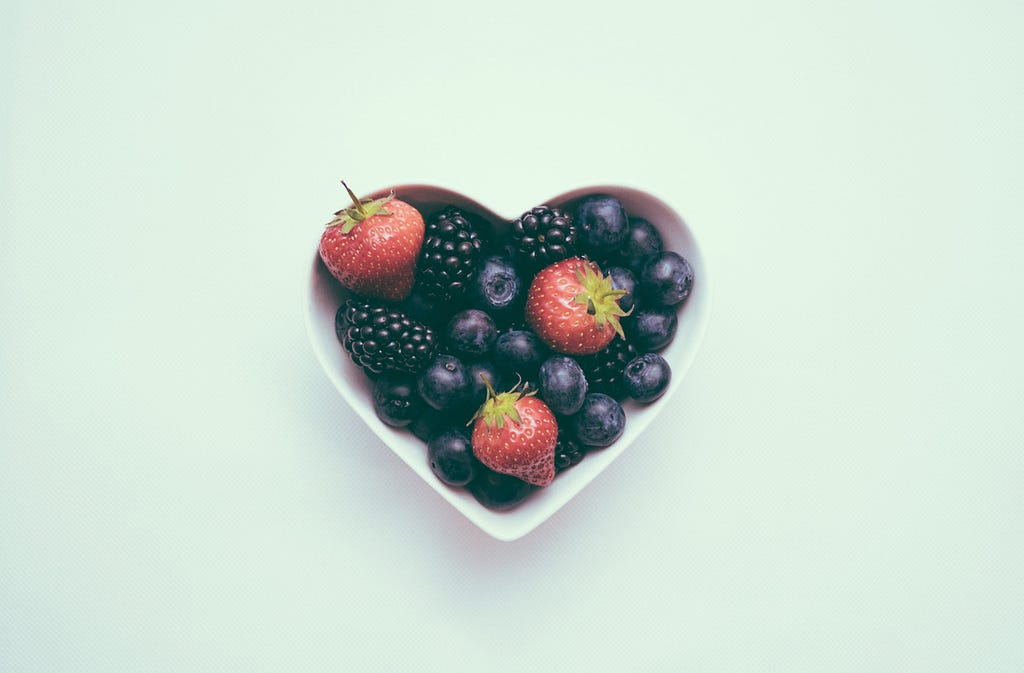 berries in a heart shaped bowl on a teal background