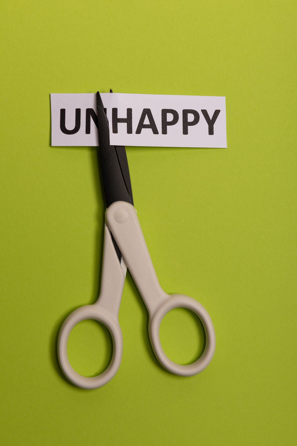 A pair of scissors cutting the word “unhappy”