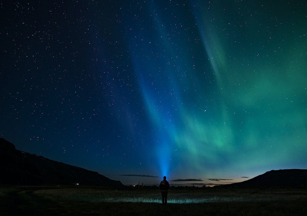 A sillfoutted person standing admiring the northern lights in the night sky