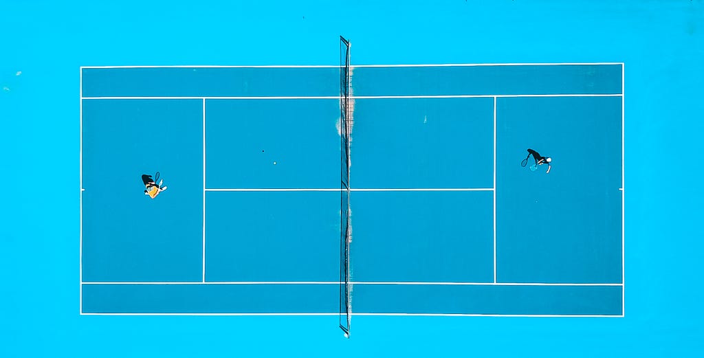 A tennis court from above. There is a player on each side of the net.