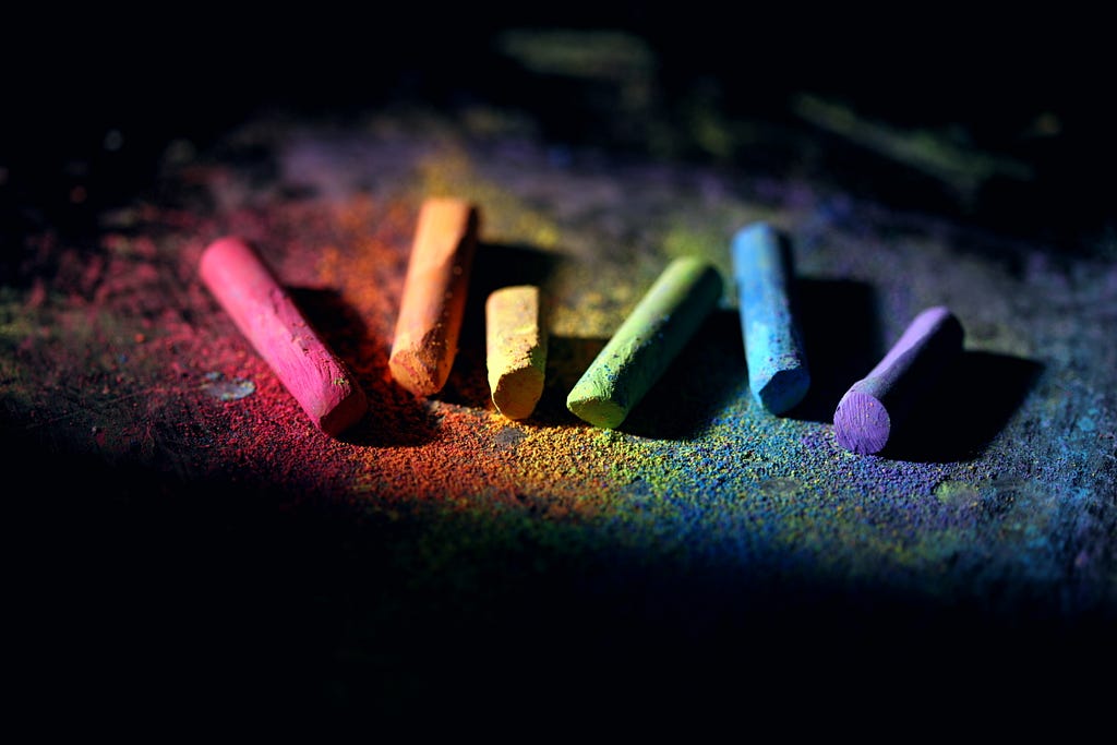 A black background with etched with six different coloured crayons with each crayon lying on the colour it painted.