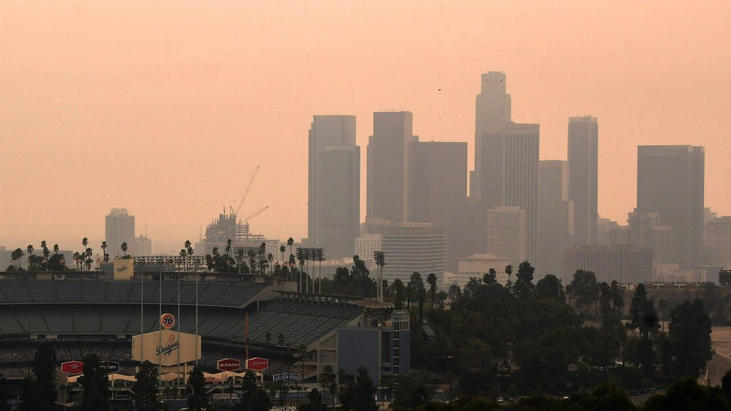 A view of downtown L.A over the shoulder of Dodger Stadium, on a hazy with a peachy orange sky.