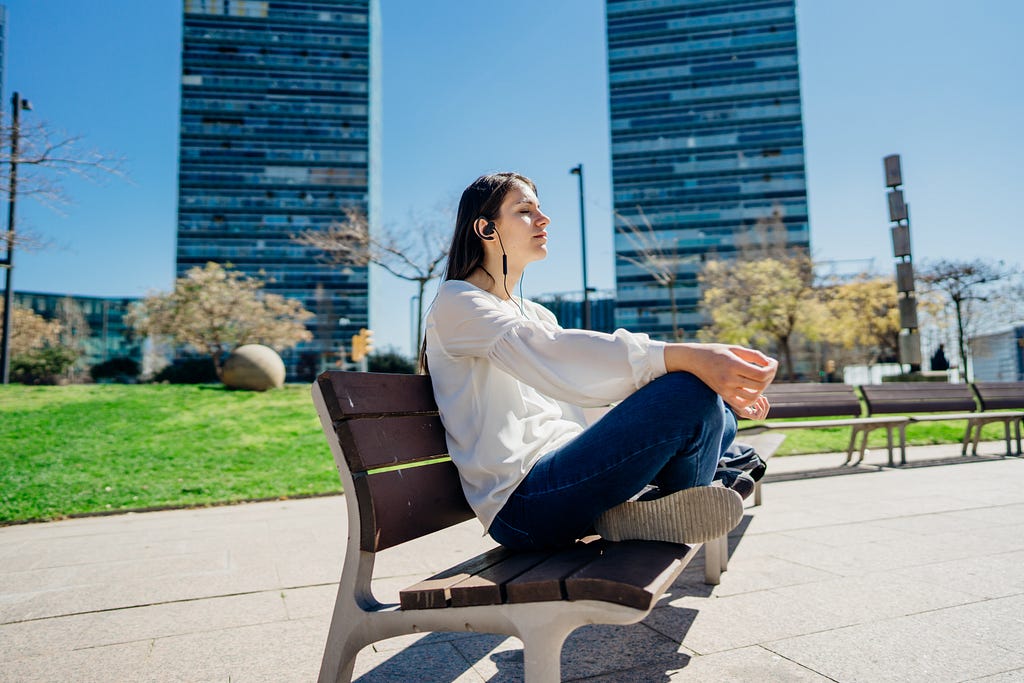 A woman meditating at a park with earphones on—putting uncertainty aside.