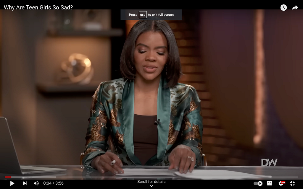 A screenshot from Candace Owens’s show on The Daily Wire. She’s in something simple and black, but over it she wears what looks like an open silk housecoat. It’s a Sacramento green with a pattern of brown owls all over it.