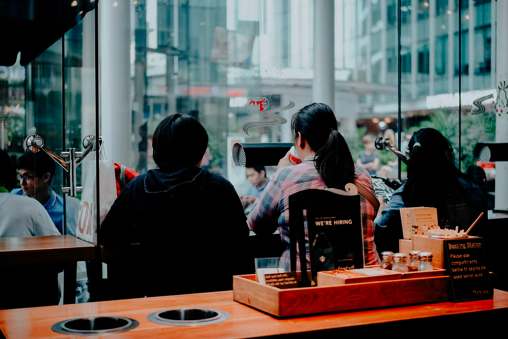 Two people sit in a coffee shop looking outside