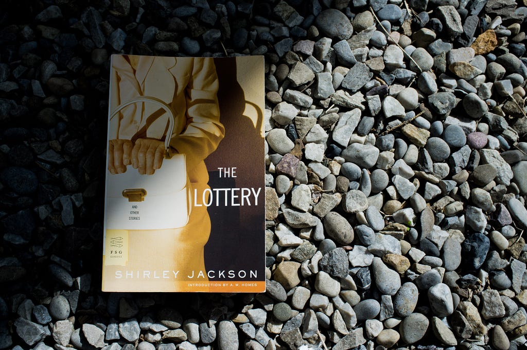 Shirley Jackson book, The Lottery and Other Stories, sitting on a bed of stones.