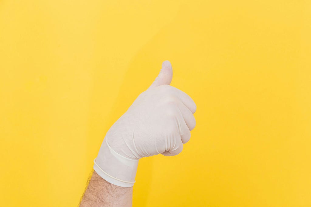 A white gloved hand gives a “thumbs up” sign of approval in front of a yellow background.