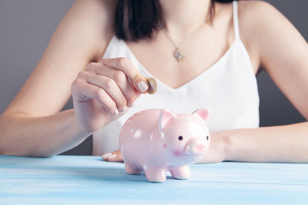 A woman putting a coin in a piggy bank.