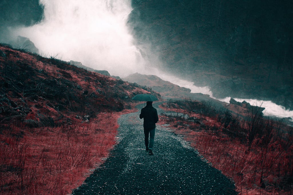 Person with an umbrella walking down a road in the rain.