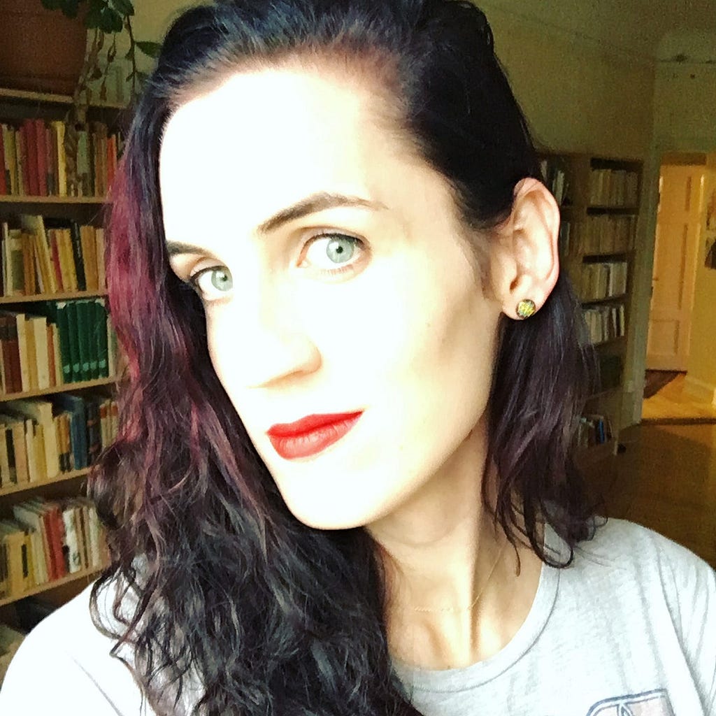Selfie with dramatic lightning, bright red lipstick, book shelves in the background.