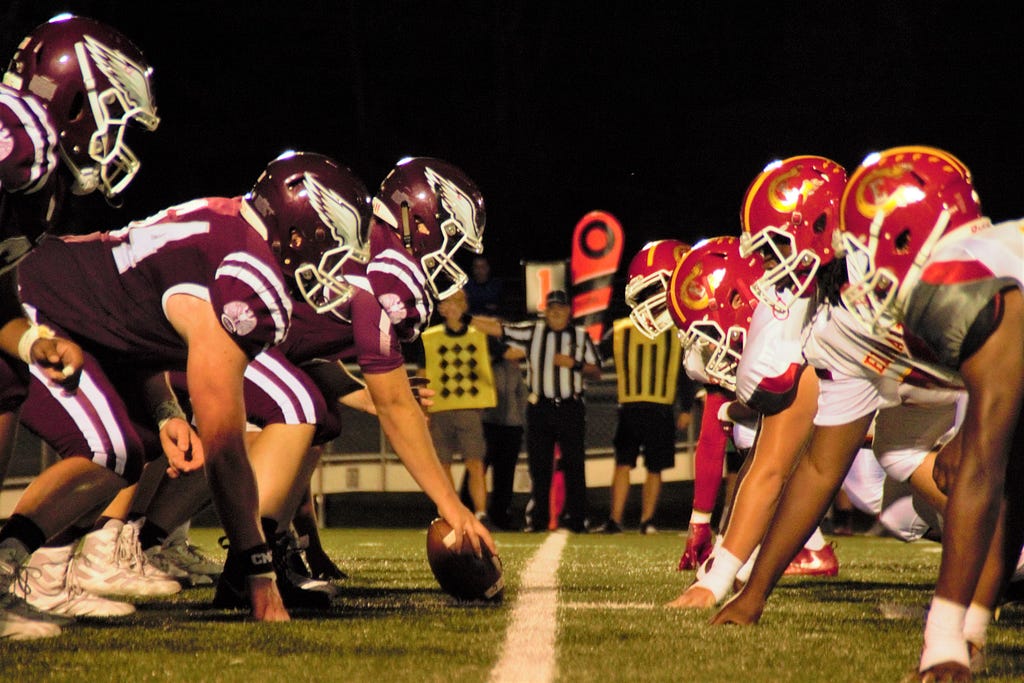 Two football teams, facing off at the line of scrimmage in a game ready stance.