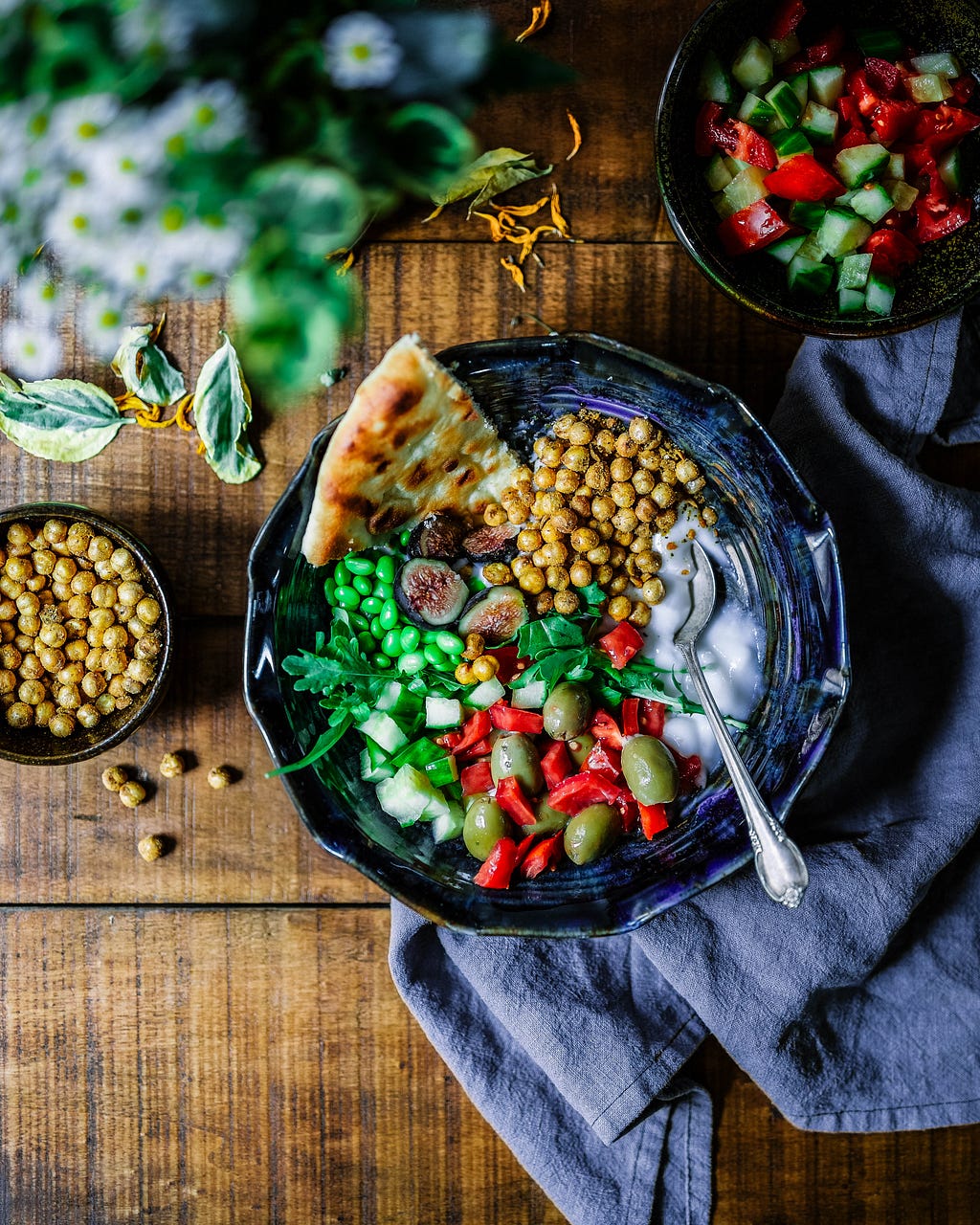 A bowl of vegetables, naan, and coconut milk on a brown table over a blue towel.