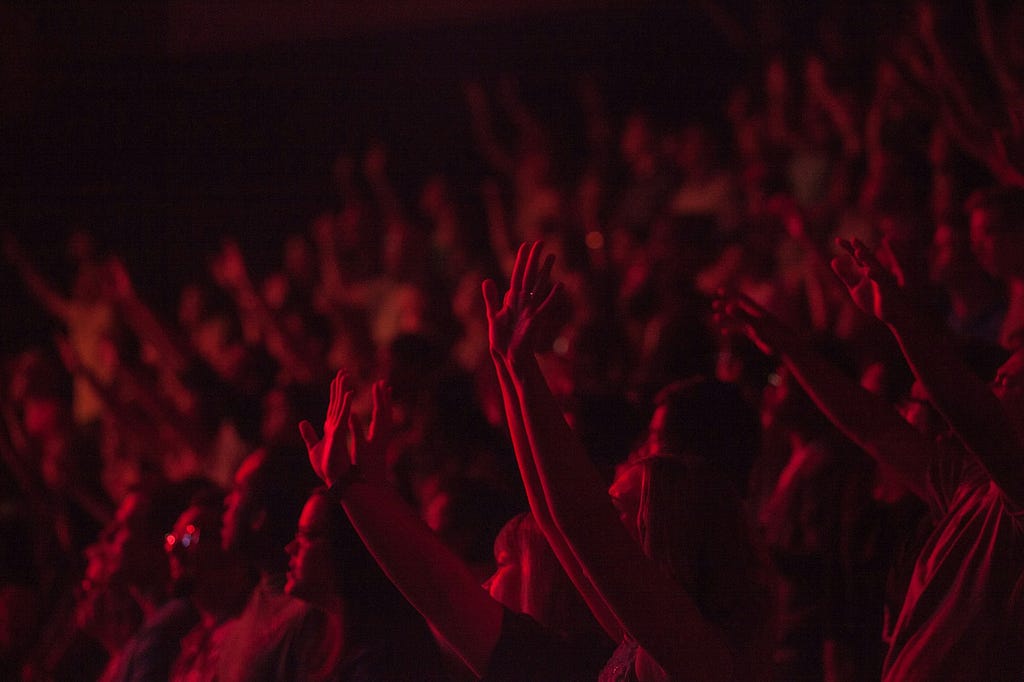 Photo of crowd in a concert, people raising hands. Photographed in a dark environment.