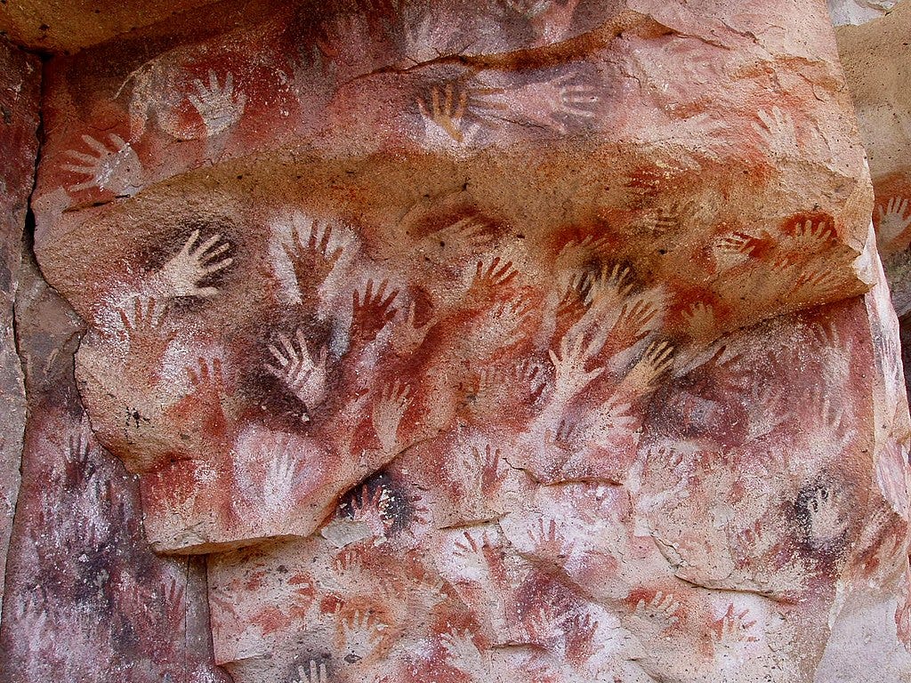 Handprints of a cavemen on a cave, made from spraying something to the cave with hands sticking to the wall, leaving marks.