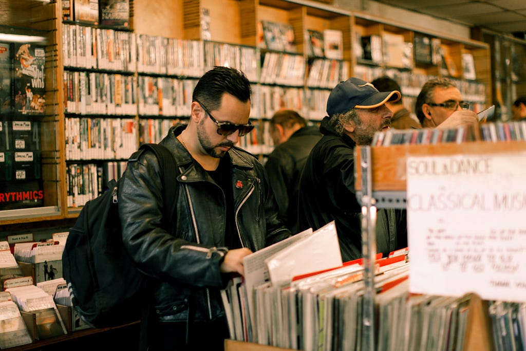 Photo of a man browsing through vinyls in a crowded record store. Photo by Marc Fanelli-Isla on Unsplash