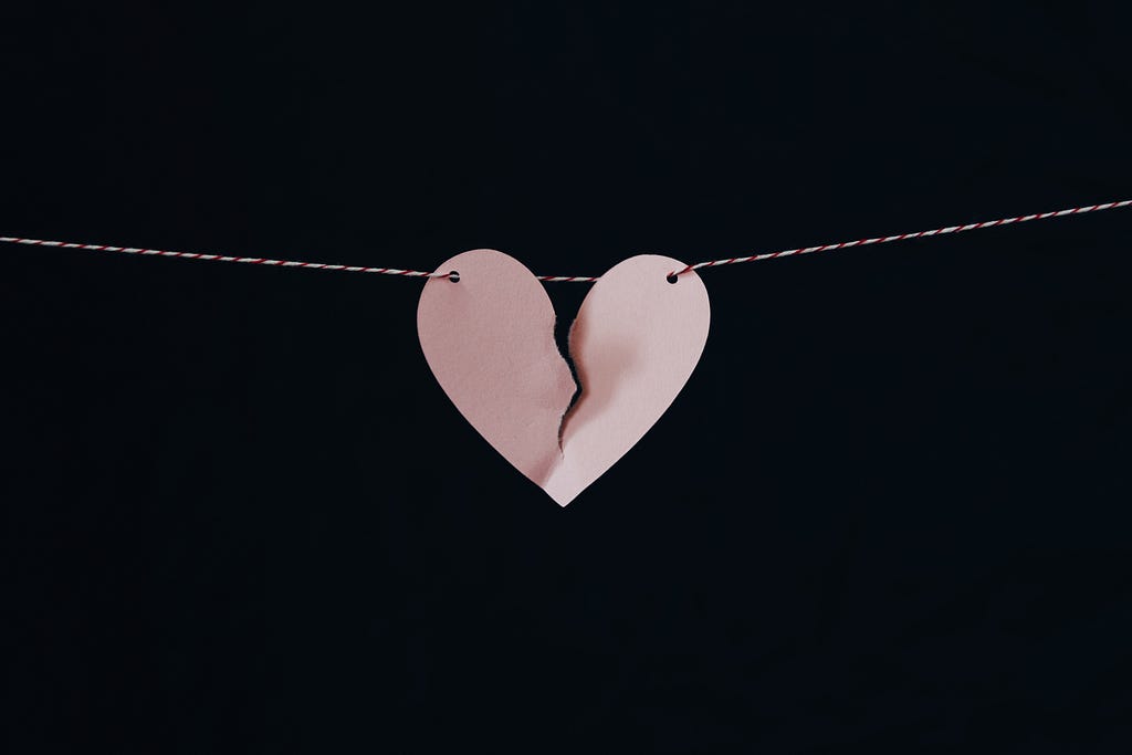 Paper heart suspended on a horizontal string tearing into two pieces