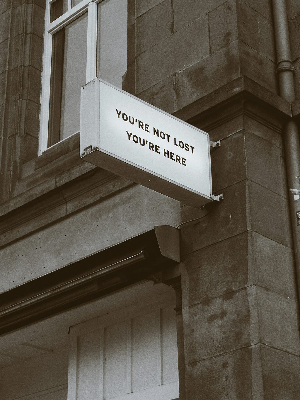 A grayscale photo of a building with a sign that reads “You’re not lost. You’re here.”