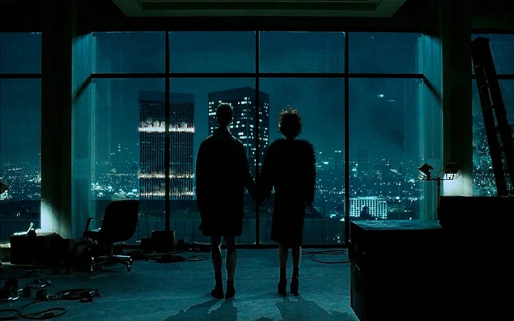 Scene from Fight Club movie. A cinematic scene featuring two figures standing hand in hand in a dimly lit room with large windows. The view outside reveals a sprawling cityscape illuminated by city lights at night. The interior is sparsely furnished, with a few scattered items and an office chair visible. The atmosphere is moody and atmospheric, evoking a sense of intimacy and contemplation.