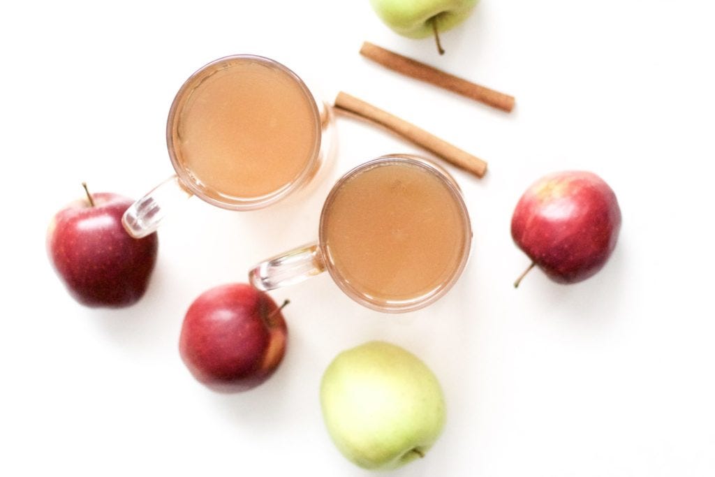 two mugs of hot cider surrounded by cinnamon sticks and apples