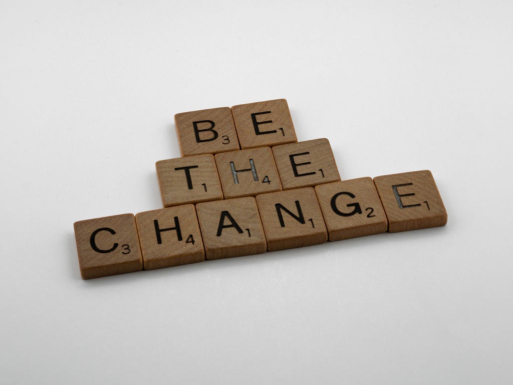 Wooden Scrabble tiles spelling out “Be the Change”.