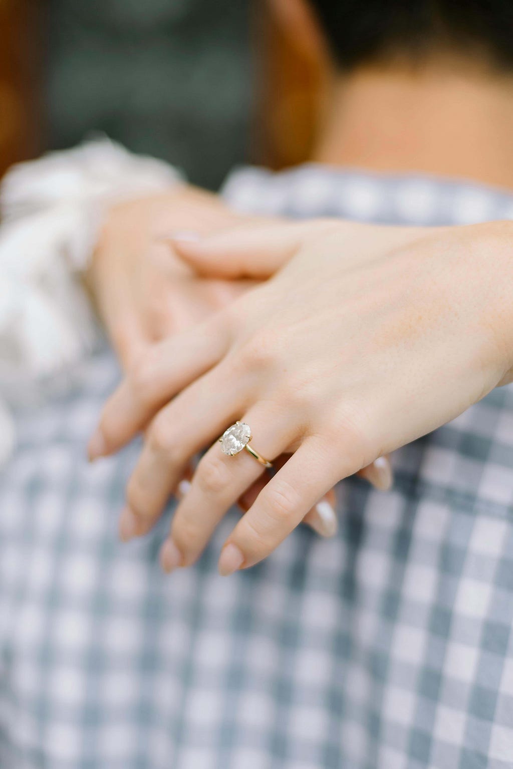 A women’s hands wrapped around her hudbands neck showcasing a beautiful diamond engagement ring.