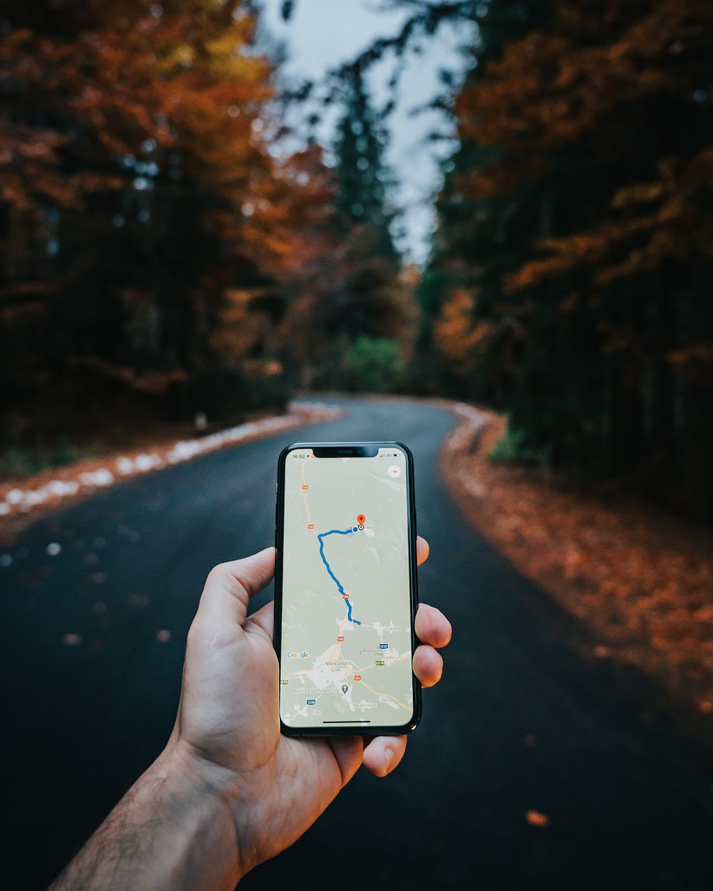 A hand holding a cellphone with a map open and a route mapped out.