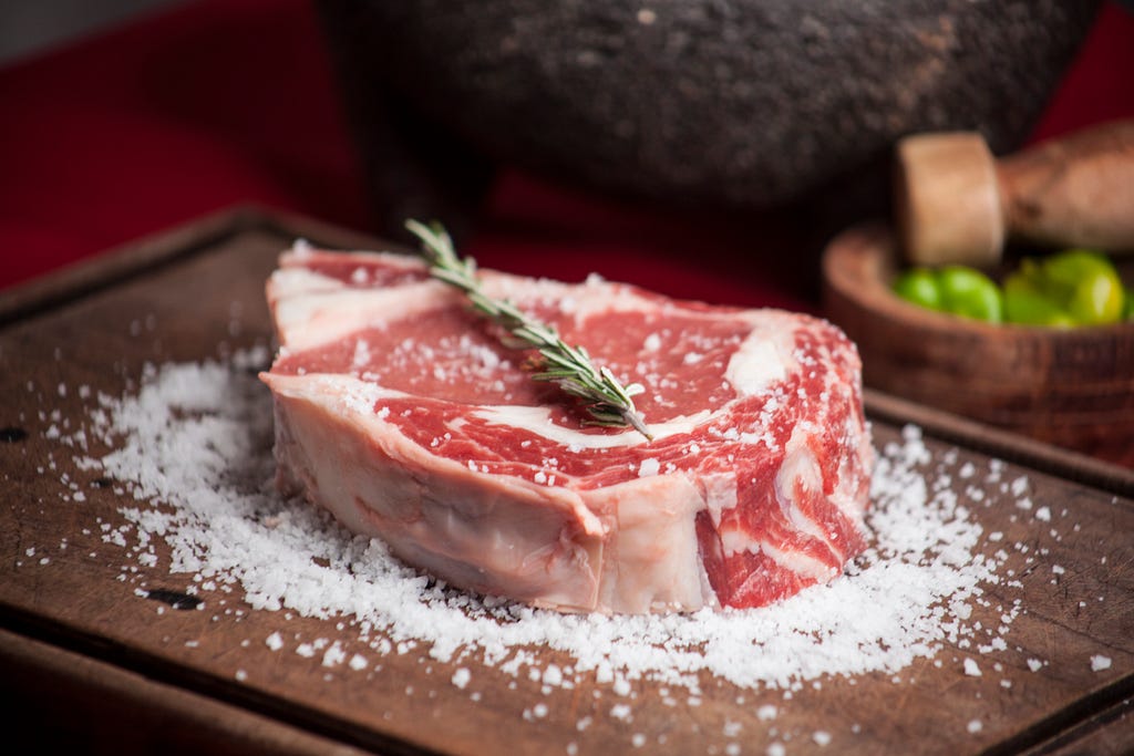 A raw steak over a cutting board covered in salt and rosemary