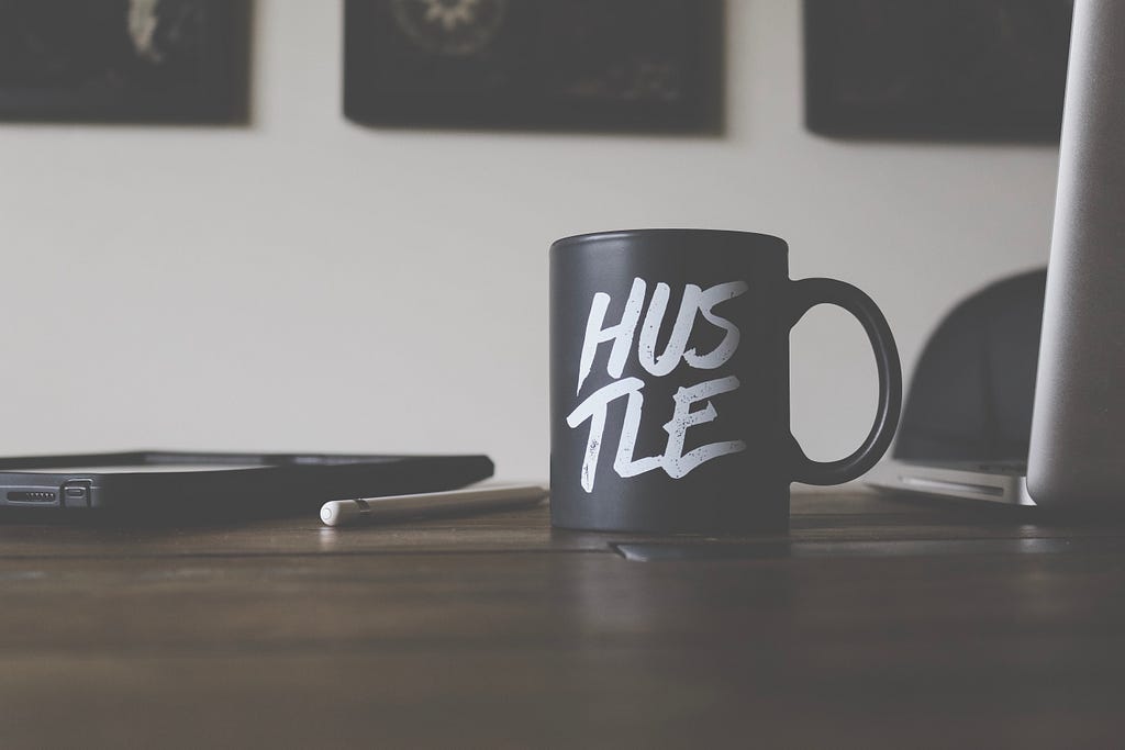 A black coffee cup with the word “Hustle” written in white text