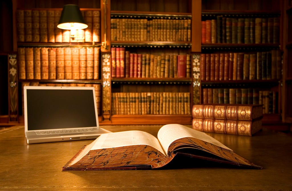 Classic library setting, an open laptop and an open book on the table