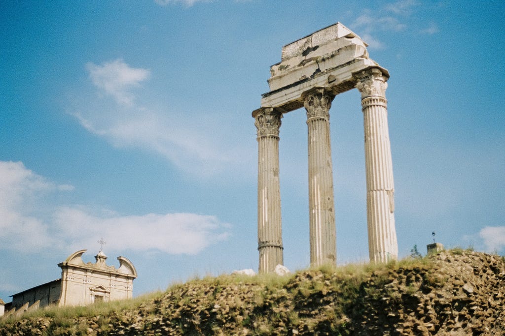 Three columns from a Roman ruin stand tall in front of a blue sky.