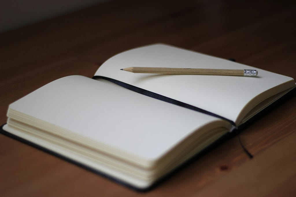 Photo of an open, blank journal with a pencil on top of the right-hand-side page.