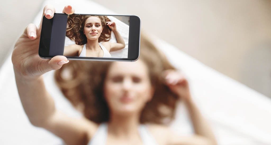 Woman lying in bed taking selfie on phone