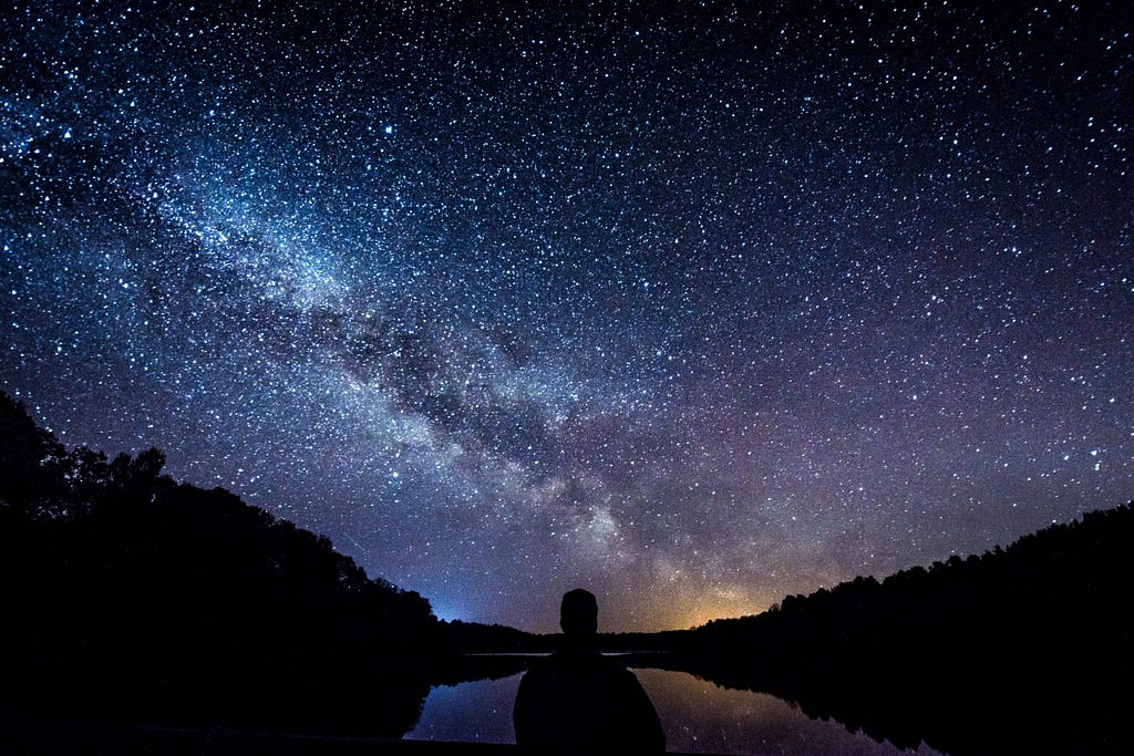 A lone figure stares at starry sky above.