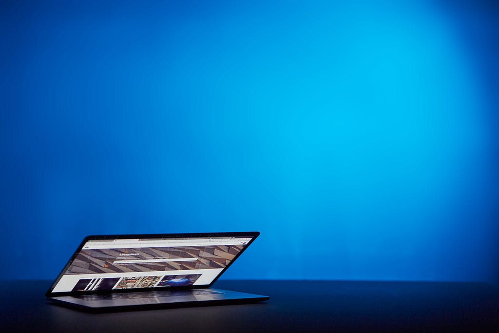 Partially open laptop with a blue backdrop.