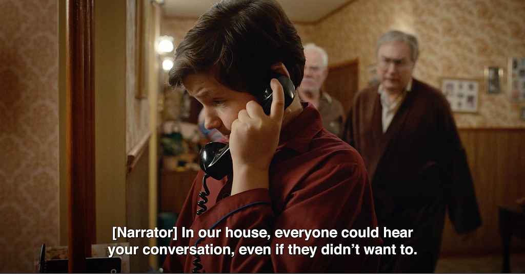 Scene from the show Son of a Critch. Set in 1985, a young Mark Critch has picked up a black, rotary phone. His father and grandfather are approaching him. The caption reads the narrator’s voice over: In our house, everyone could hear your conversation, even if they didn’t want to.