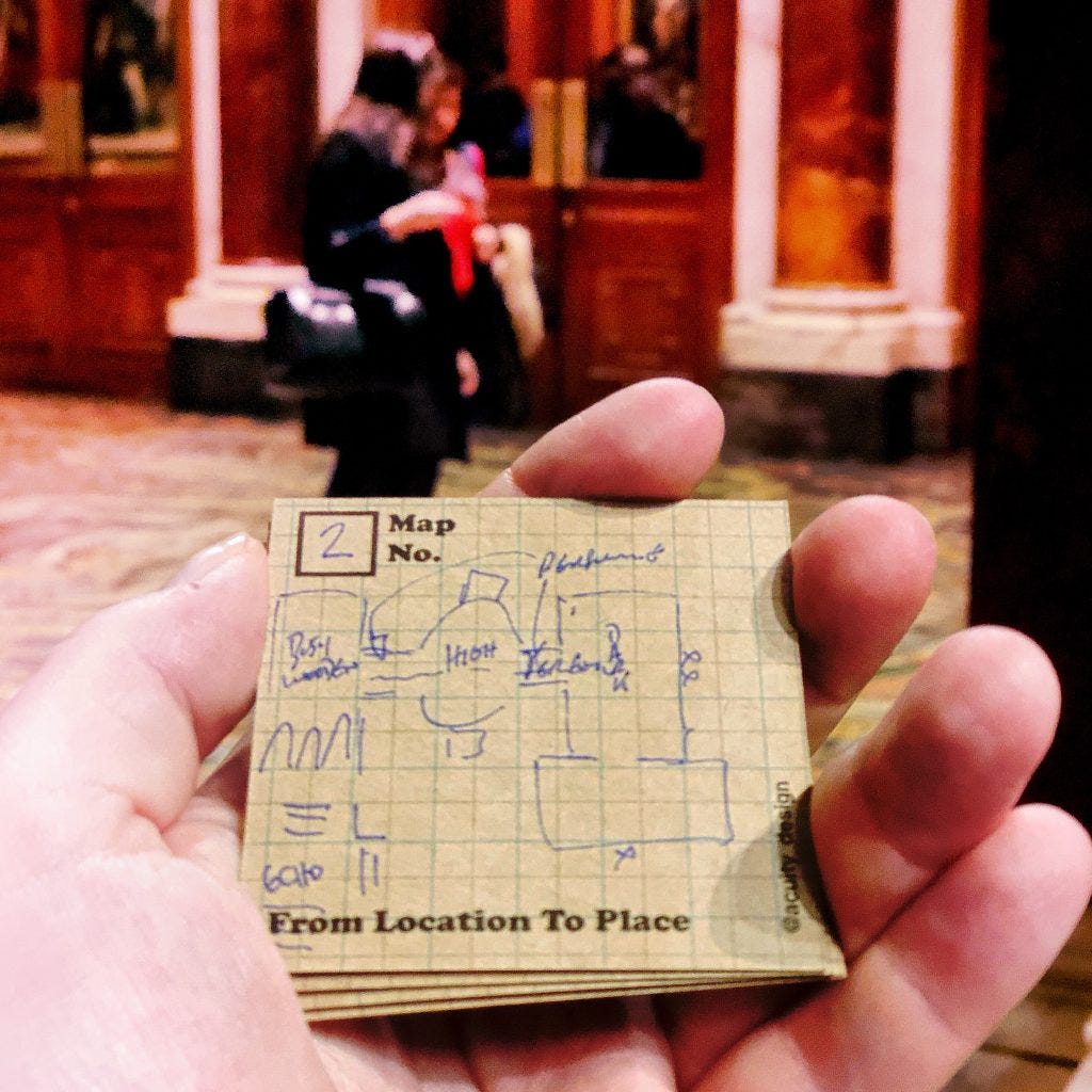 Mini postcard in hand with sketch map of gallery while people walk in front of portraits in the distance