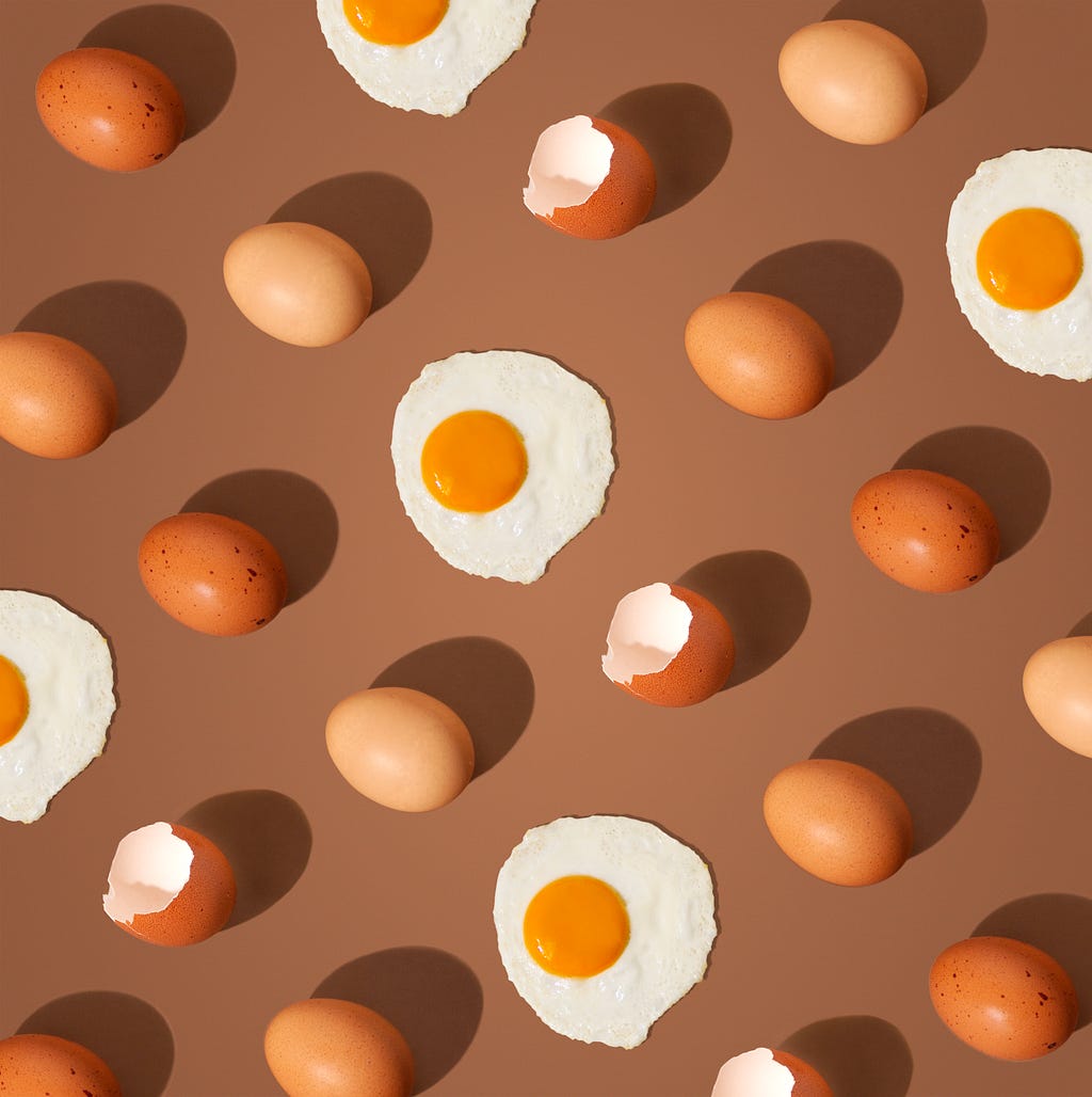 Mosaic of brown eggs in shell alternating with fried eggs on brown background.